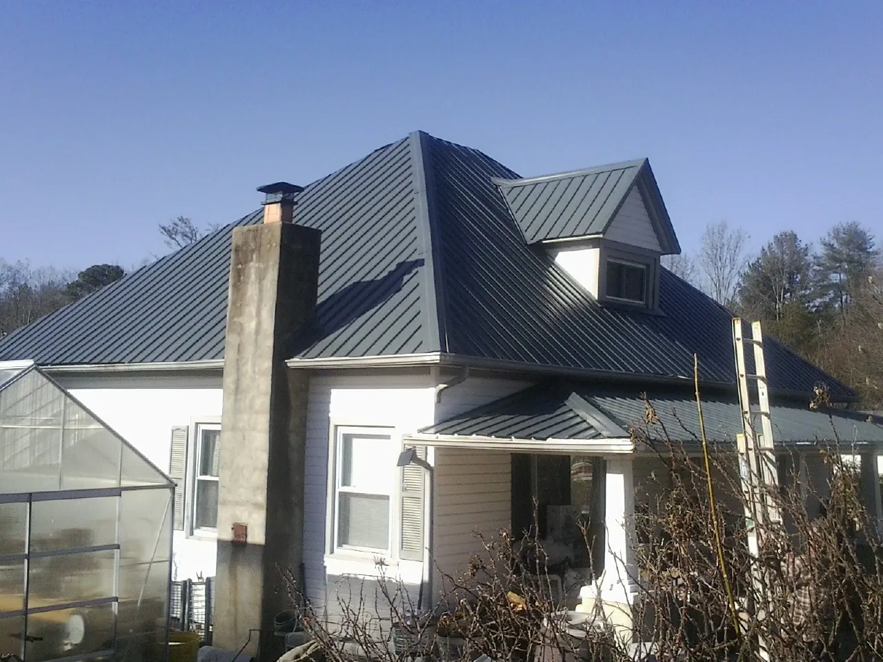 Dark blue standing seam metal roof on a white farmhouse with dormer — Slate & Tile Roof Repair by Roofing Brothers in Campobello