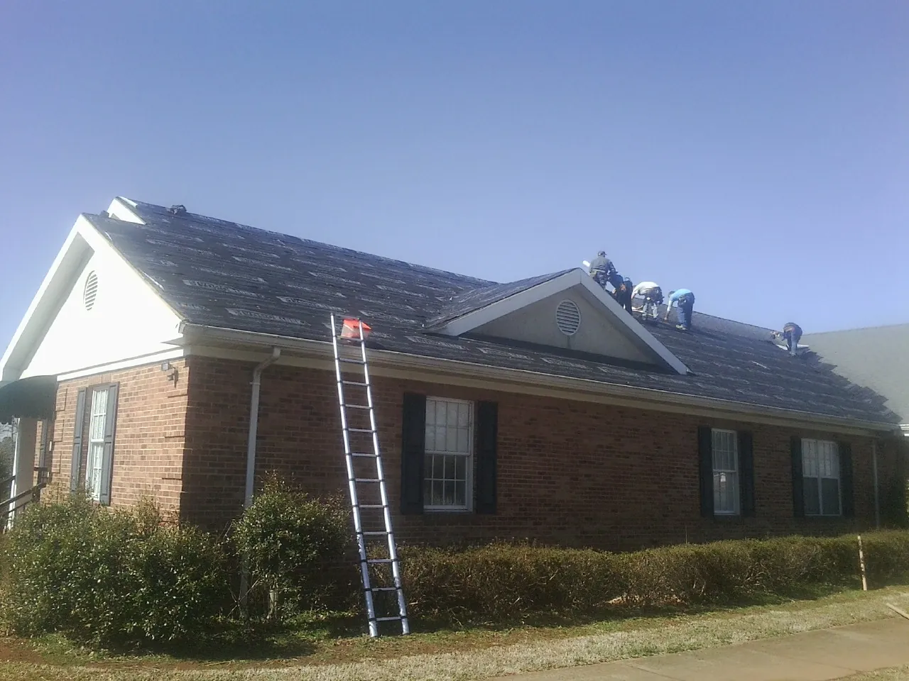 Crew tearing shingles off a brick ranch roof with a ladder set — Metal Roof Repair work by our crew in Campobello