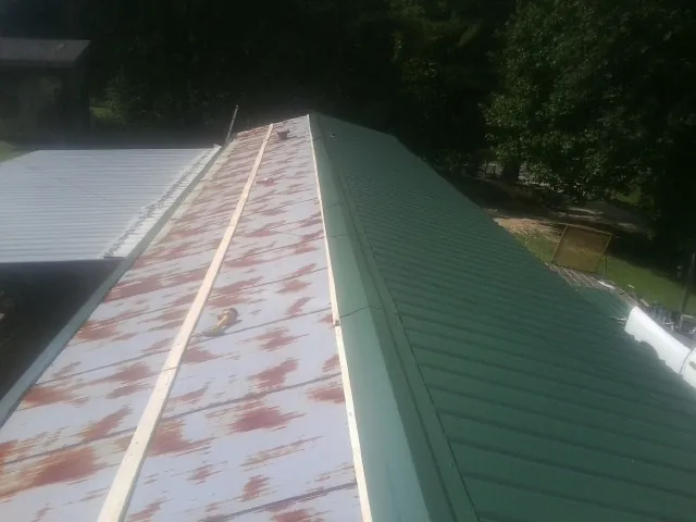Old rusted panels beside newly installed green metal roofing — Wind Damage Roof Repair by Roofing Brothers in Campobello