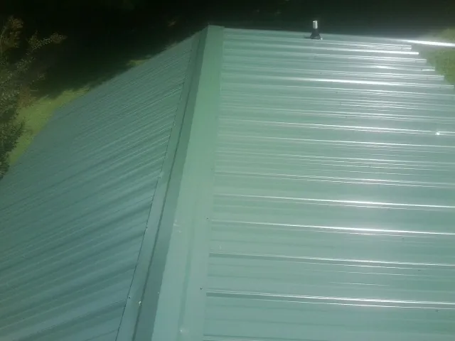 New green metal panels meeting at the ridge of a roof — Flat Roof Repair work by our crew in Campobello