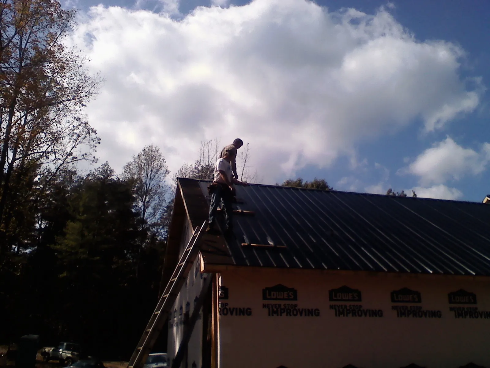 Roofer fastening dark metal panels high against a cloudy sky, from a Roof Inspection job in Campobello