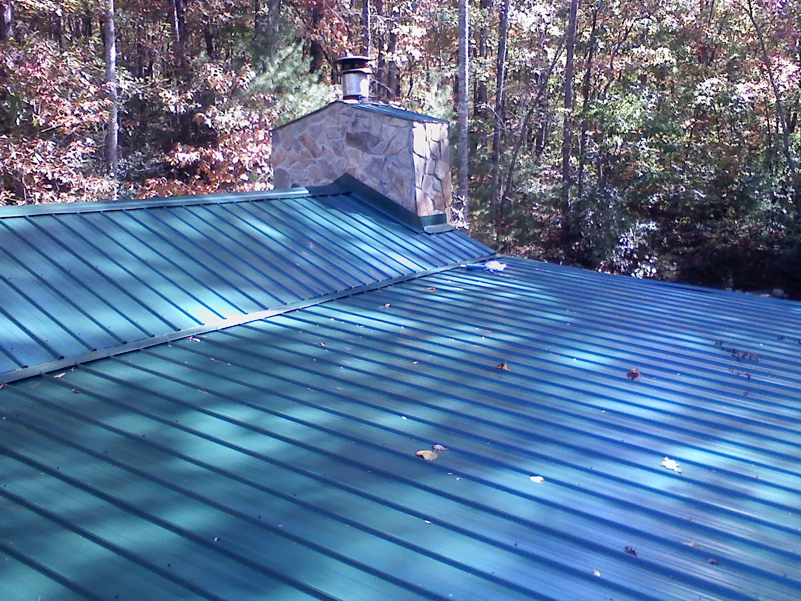New green metal roof and stone chimney surrounded by autumn woods in Campobello