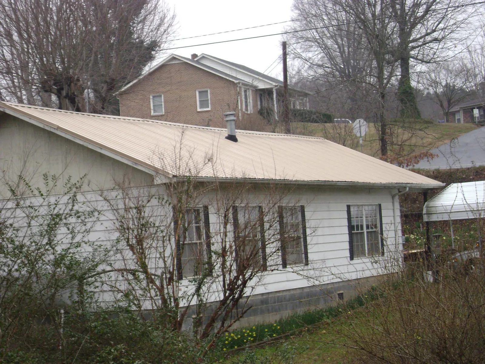 Tan metal roof on a white sided house set into a hillside — Commercial Roofing by Roofing Brothers in Campobello