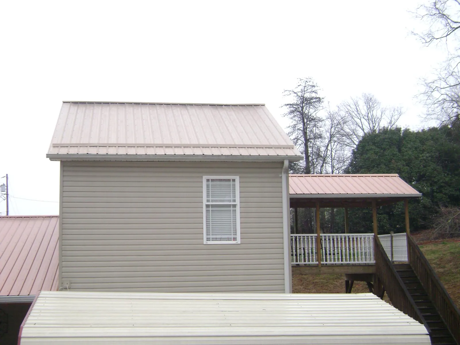 Tan metal roofs on a two story addition and attached porch, from a Roof Replacement job in Campobello